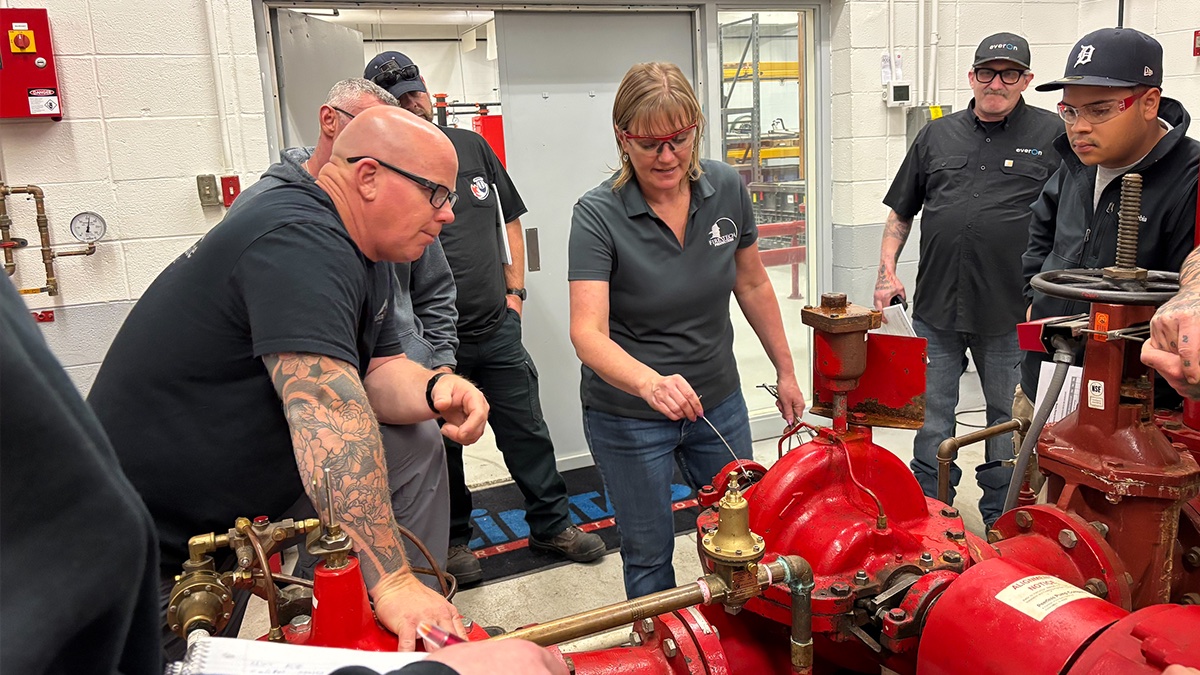 A hands-on class gathered around a fire pump and its valves at Fire Tech