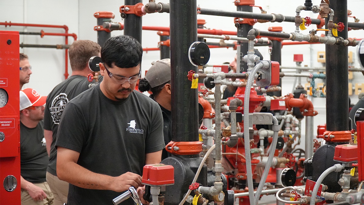 A Fire Tech student working on sprinkler riser valves in the training lab while classmates look on