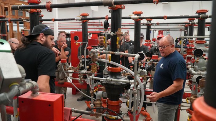 A Fire Tech instructor explaining a sprinkler riser to a group of students in the training lab