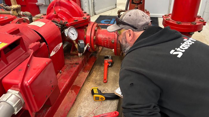 A student leaning in to inspect a fire pump and its pressure gauge during a hands-on class