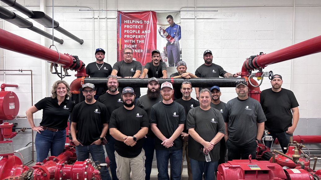 A full class of Fire Tech workshop attendees and instructors standing together in the fire pump training room
